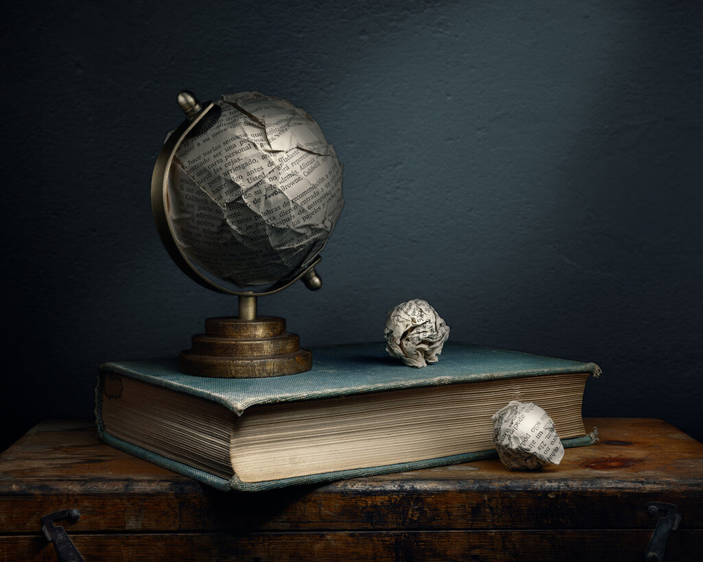 Fotografía fine art de bodegón con globo terráqueo deformado de papel sobre libro antiguo e iluminación lateral