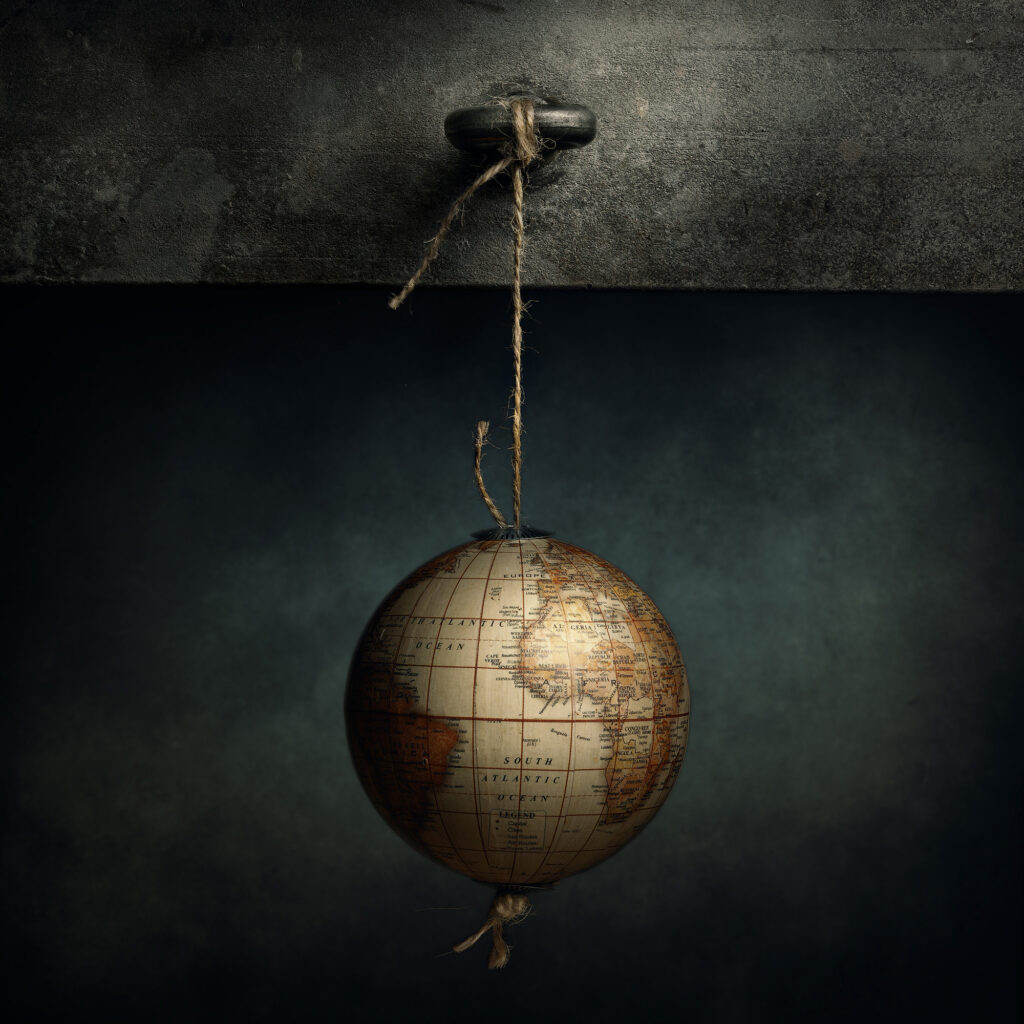 Bodegón conceptual con globo terráqueo colgado de una cuerda sobre fondo oscuro con iluminación lateral