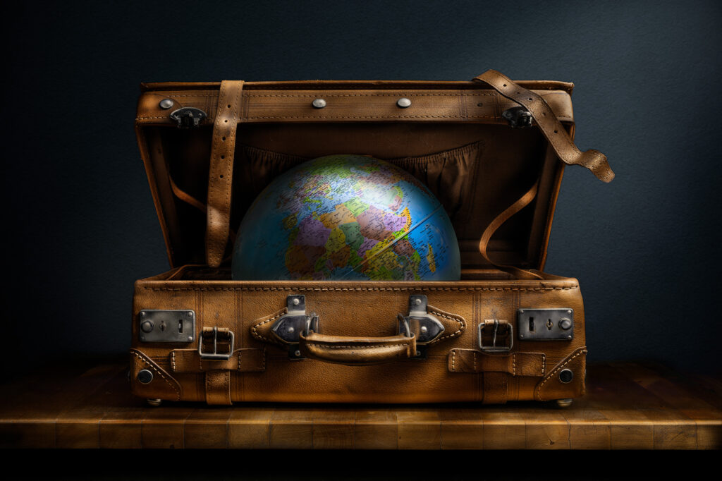 Bodegón conceptual con globo terráqueo dentro de una maleta antigua abierta sobre fondo oscuro