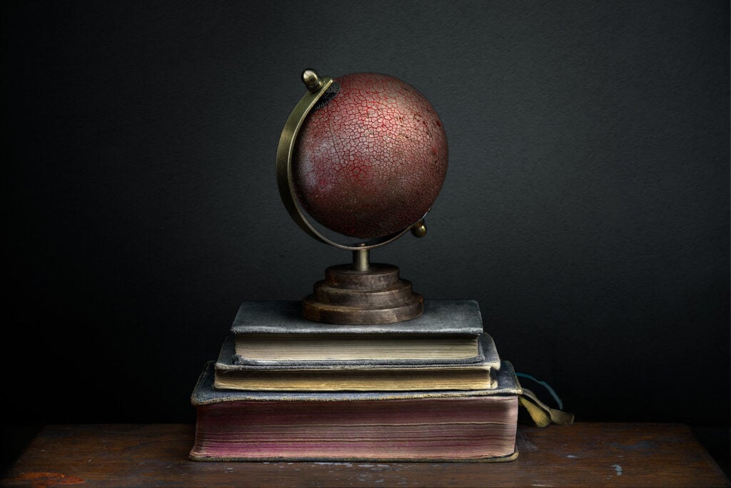 Bodegón conceptual con globo terráqueo cuarteado en rojo sobre libros antiguos y fondo oscuro