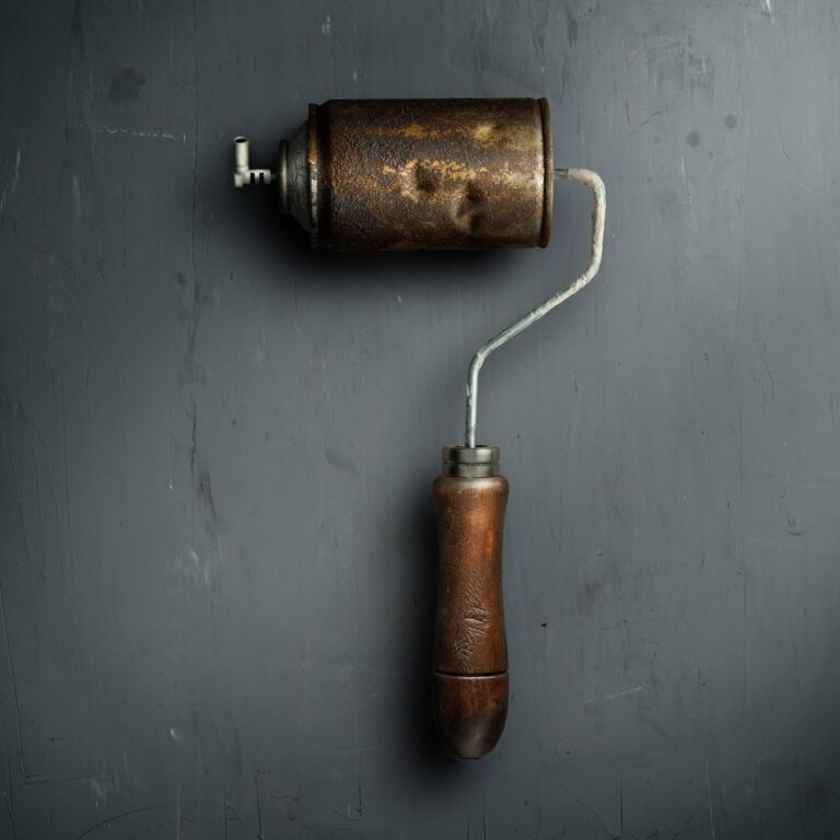 Rodillo de spray — bodegón conceptual de un rodillo de pintura industrial oxidado con válvula, iluminado con light painting sobre fondo gris oscuro