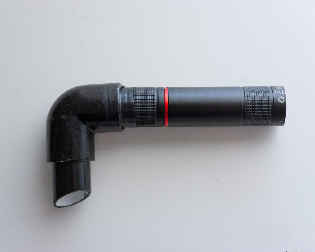 Una linterna negra con un anillo rojo acoplada a un tubo de plástico negro en forma de codo para dirigir el haz de luz en fotografía de light painting.